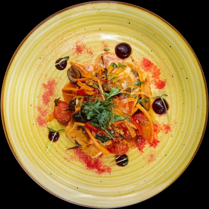 Vegetable pasta with tomatoes, peppers and olives on a yellow plate